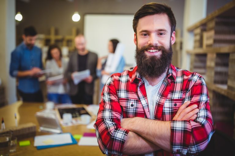 Portrait of confident businessman by table with colleagues in background at creative office