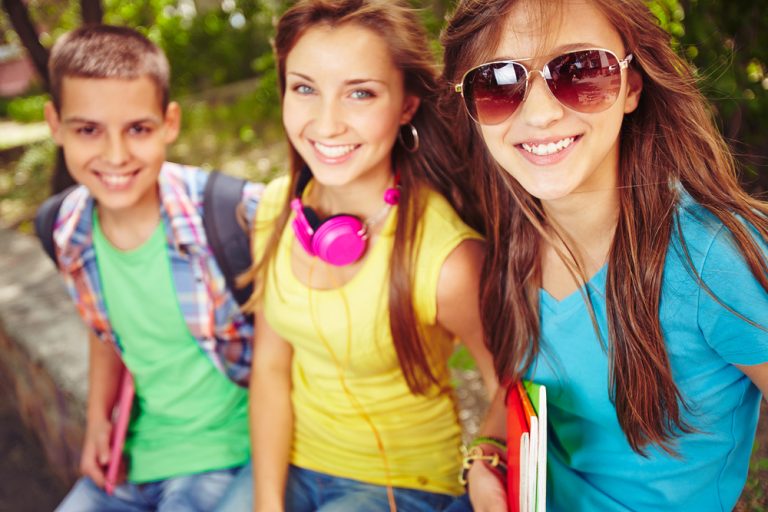 Happy teenage girls and guy looking at camera